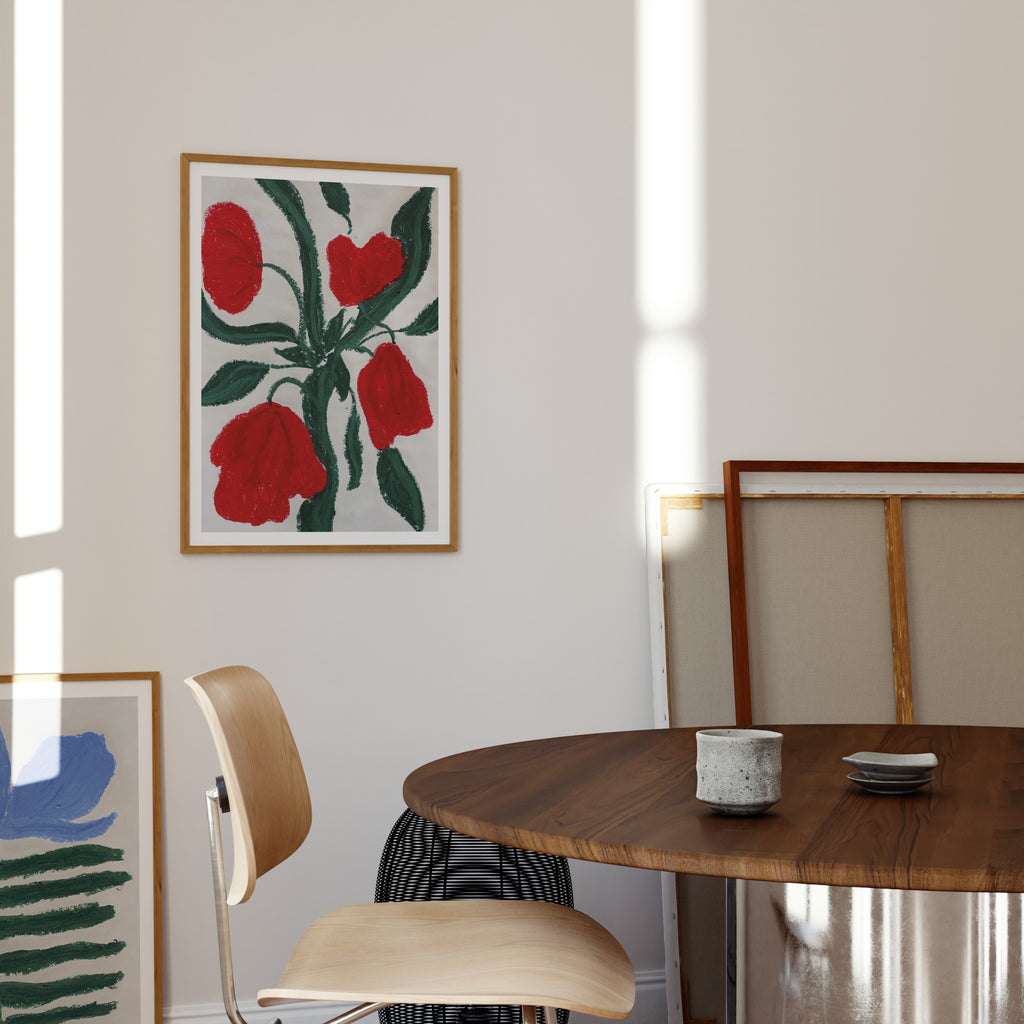 Kunstprint med røde blomster og grønne blade ophængt over spisebord i lyst og moderne hjem.