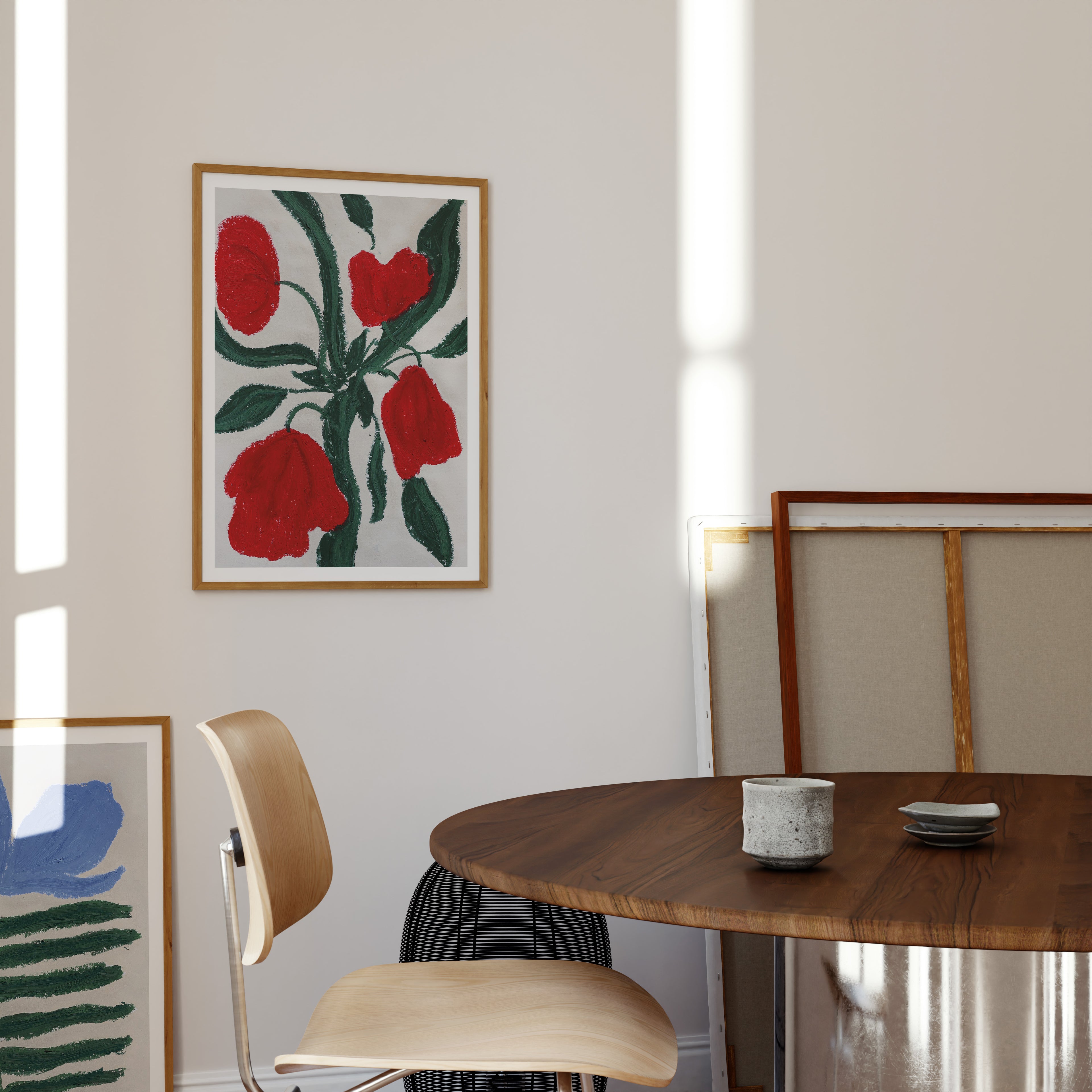 Kunstprint med røde blomster og grønne blade ophængt over spisebord i lyst og moderne hjem.